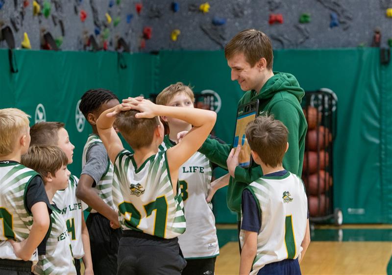 Middle school boys basketball coach talking with young players during a team huddle at New Life Academy.