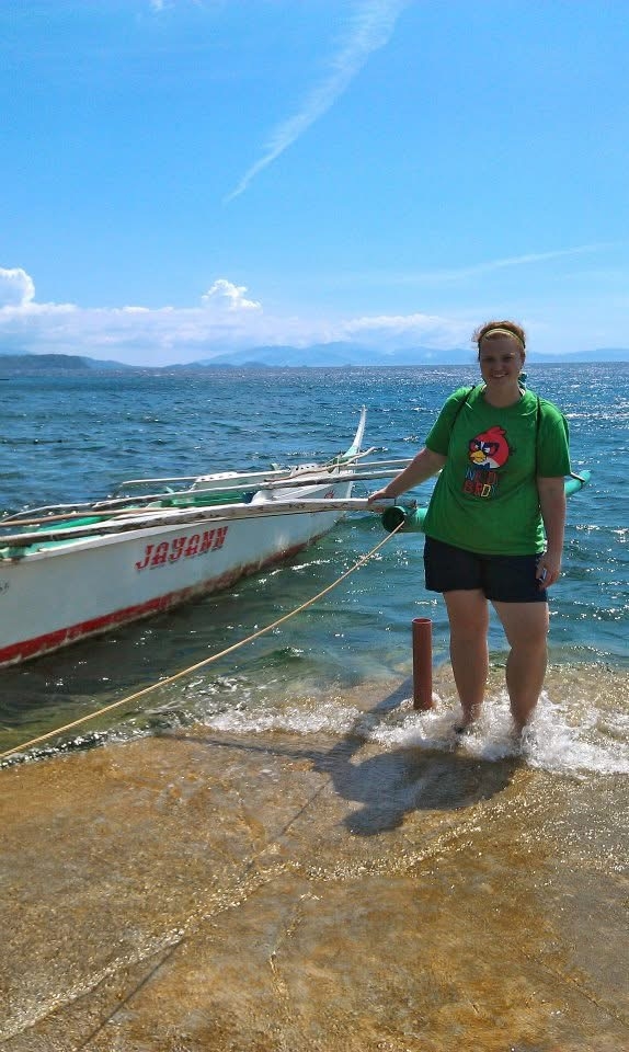 Ms. Olson standing on the shore in the Philippines beside a boat.