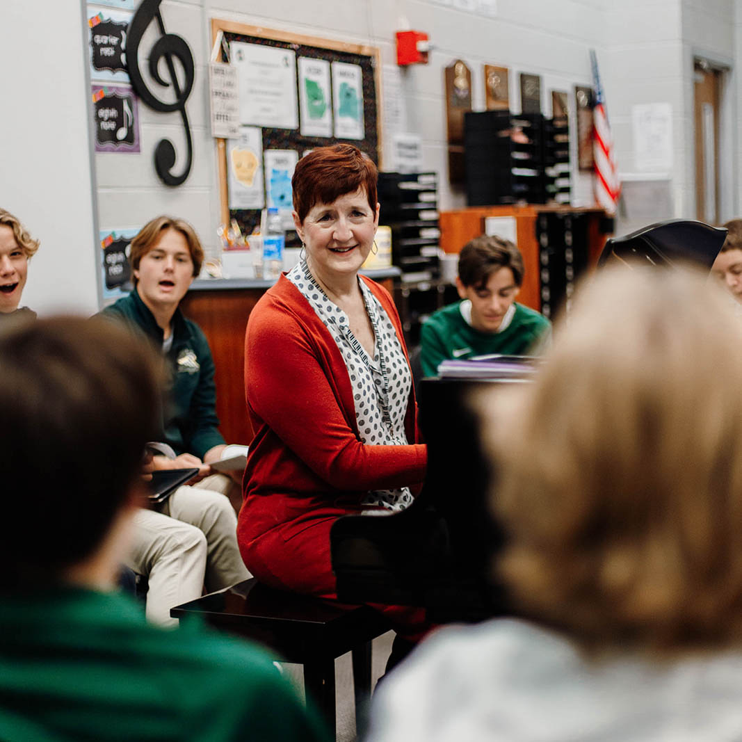 New Life Academy choir teacher leading students in a classroom rehearsal with music folders and choir room décor.