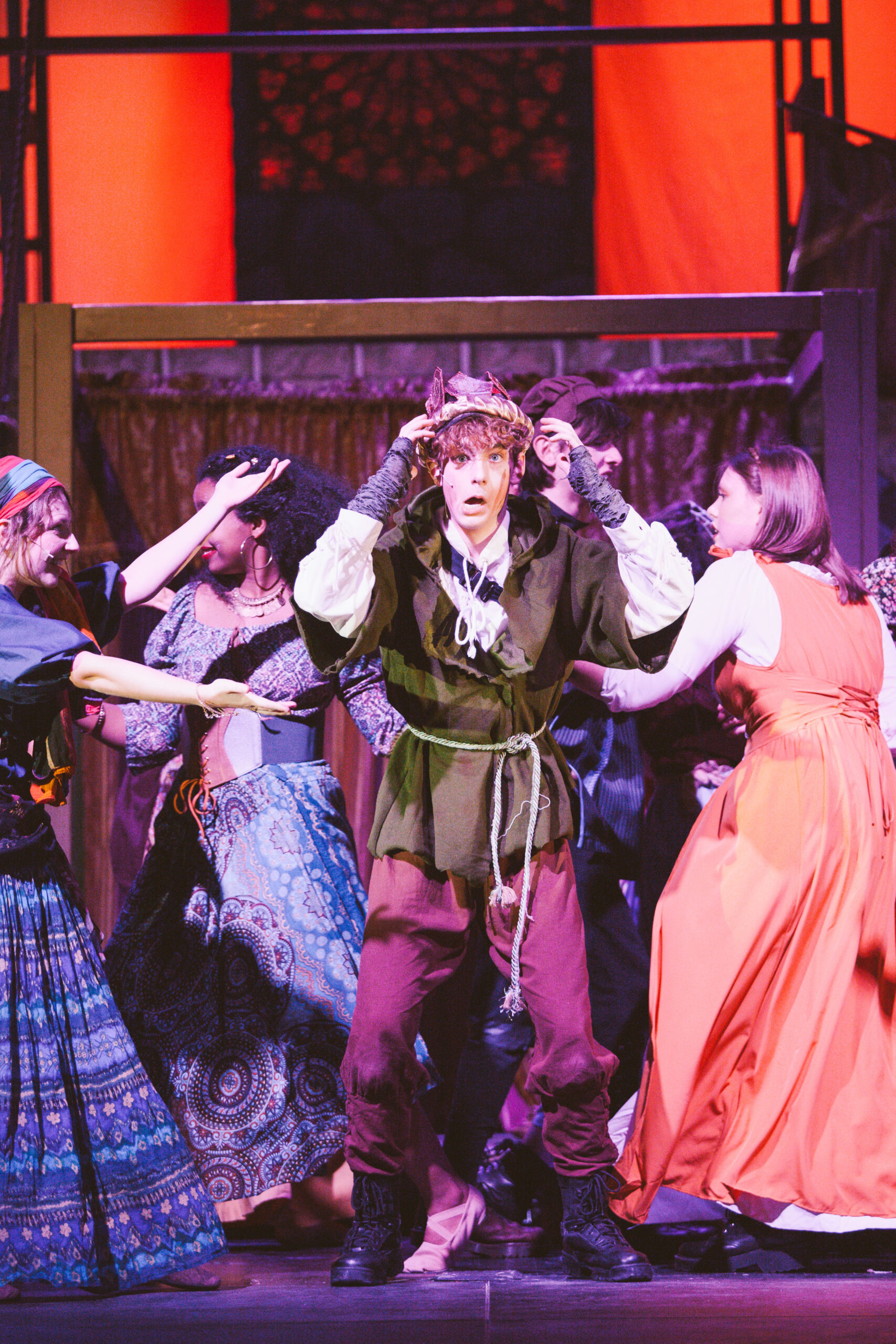 New Life Academy theatre cast performing a dramatic scene in the school’s production of The Hunchback of Notre Dame, with characters gathered on stage under warm lighting.