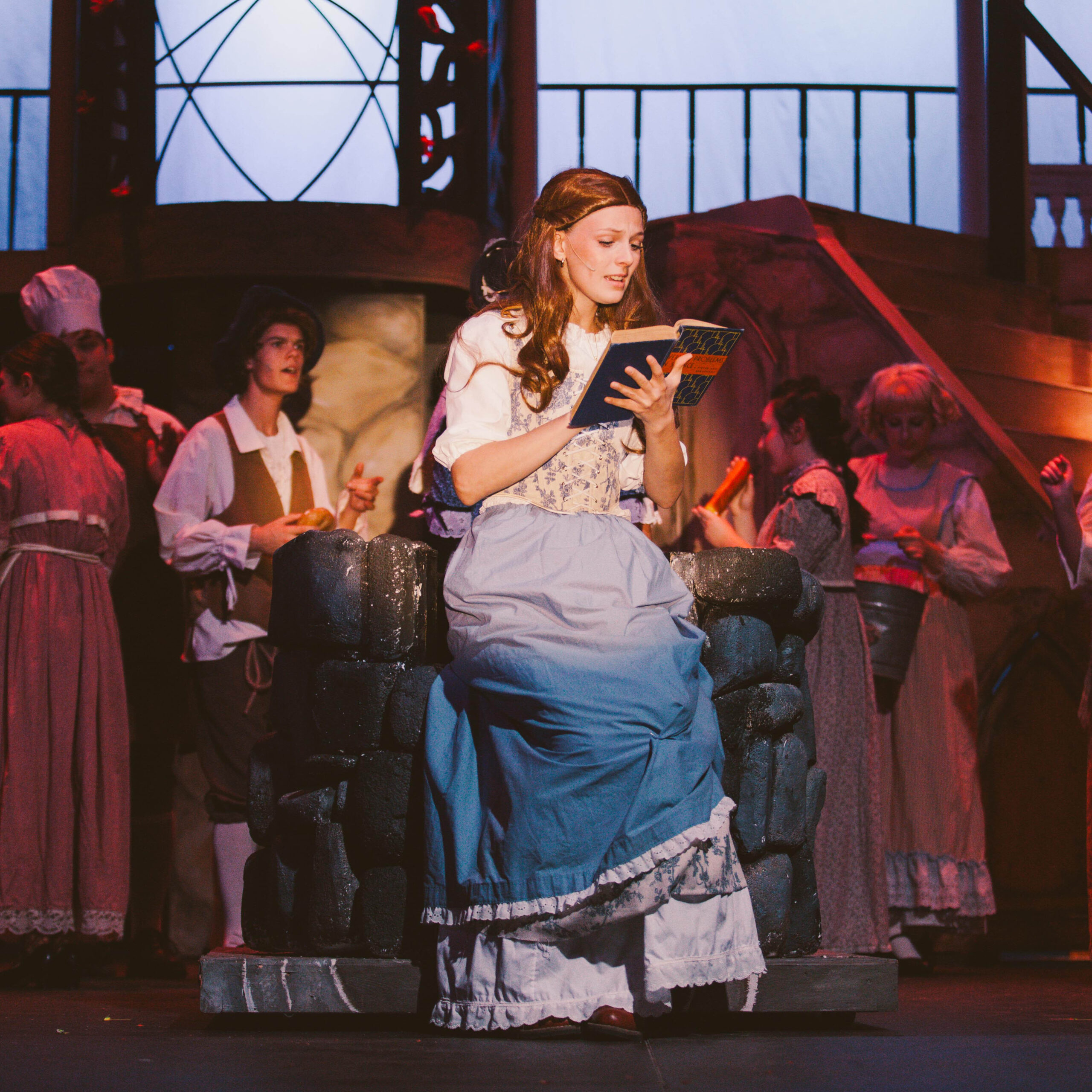 New Life Academy theatre cast member reading a book during a staged scene in the school’s production of Beauty and the Beast.