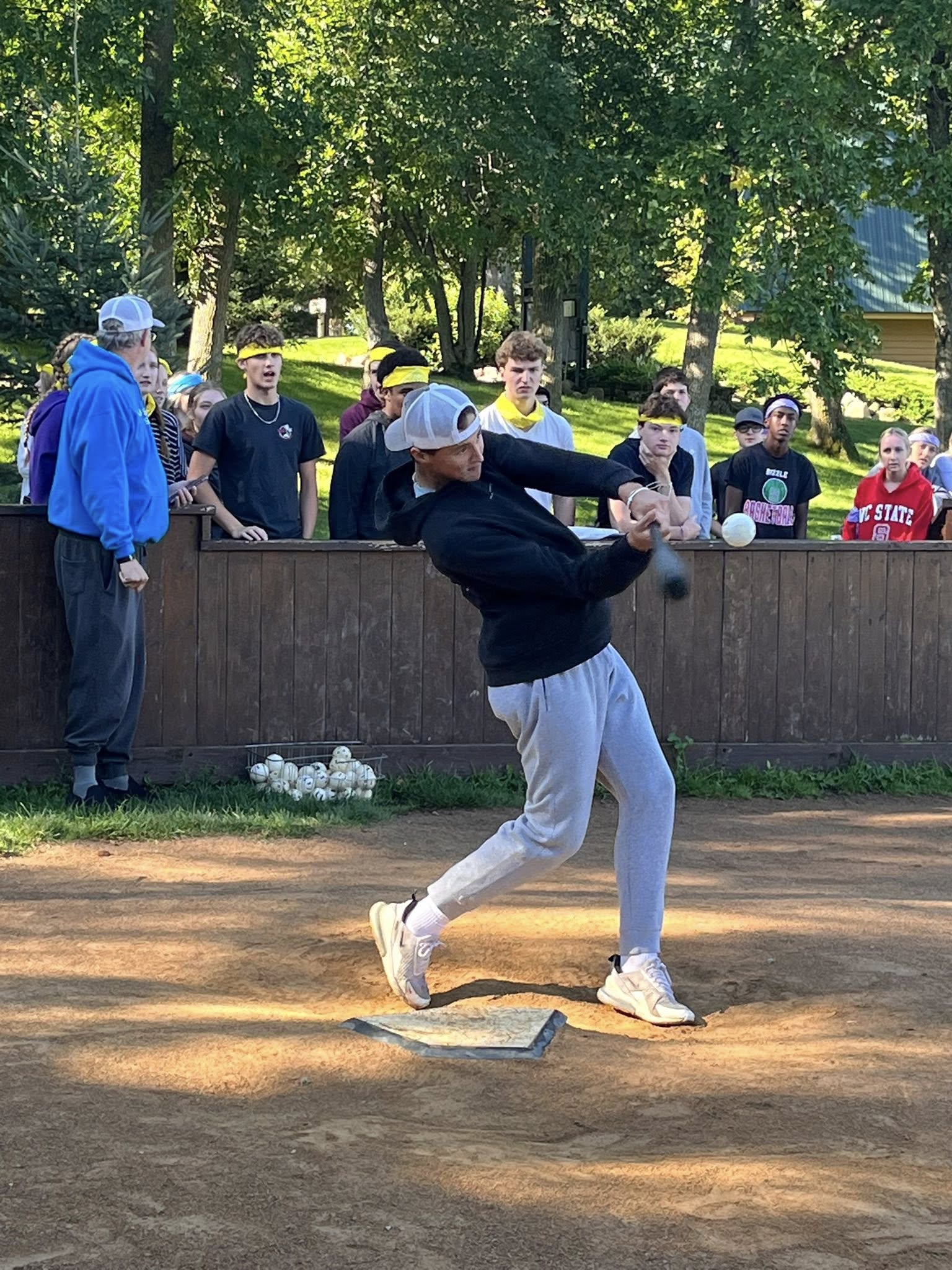 New Life Academy senior hitting a baseball with a bat during the Home Run Derby at the Senior Retreat, highlighting athletic energy and school spirit.