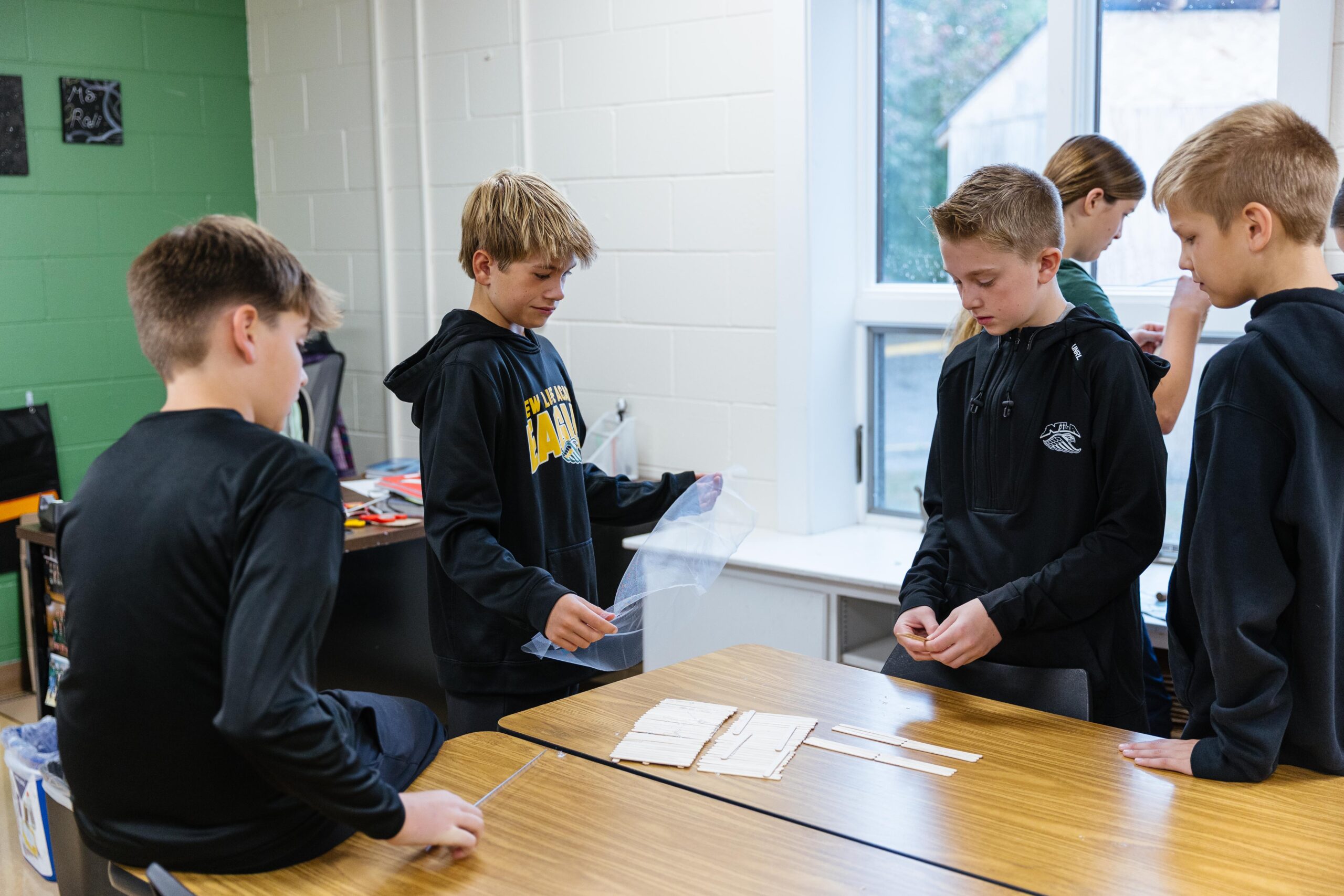 Group of middle school boys at New Life Academy work together on a science project using wood sticks and plastic to build a prototype