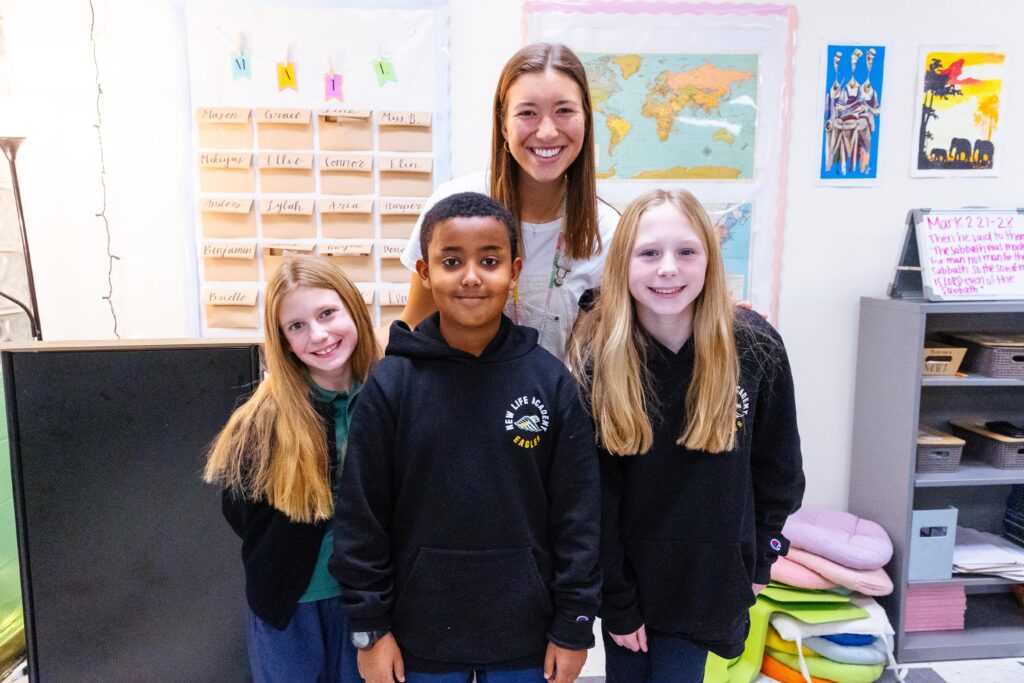 New Life Academy fifth grade classroom scene showing the teacher with several students during a class activity, featured in an article introducing new fifth grade teacher Megan Bohlig.