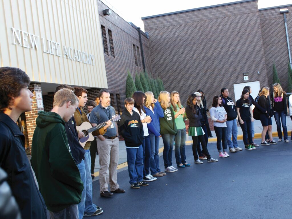 Students and staff gather in prayer outside New Life Academy, reflecting the school's Christ-centered mission.
